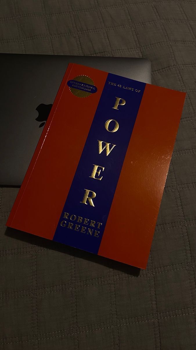 an open laptop computer sitting on top of a bed next to a red and blue book