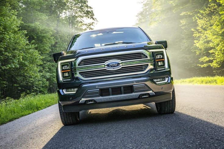 the front end of a black pickup truck driving down a road with trees in the background