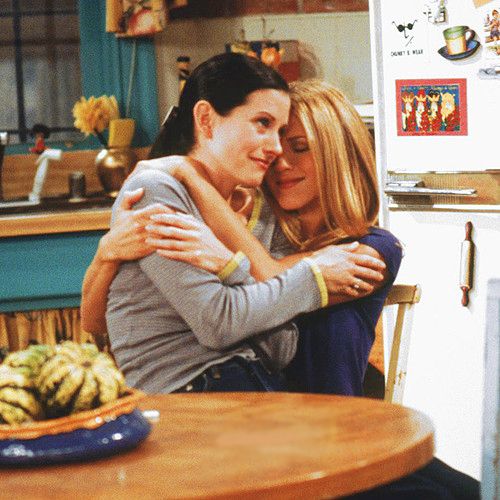 two people hugging each other at a table in front of a refrigerator and stove top