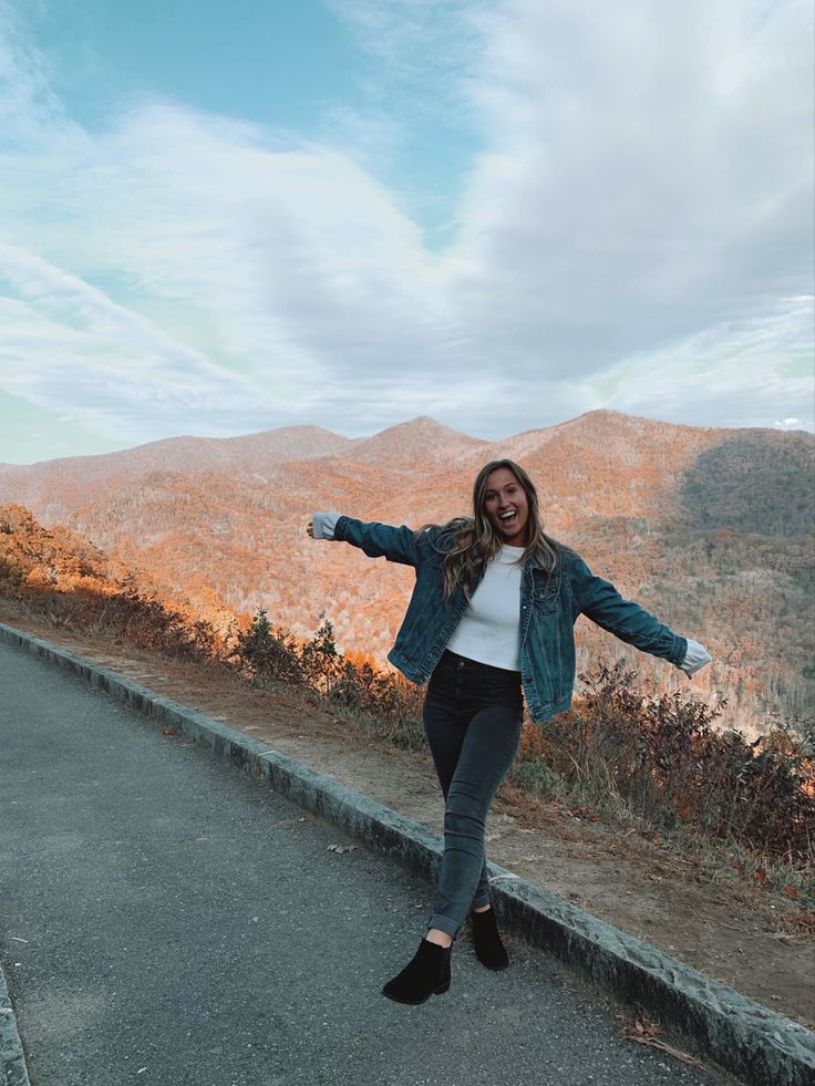 a woman standing on the side of a road with her arms spread out and smiling