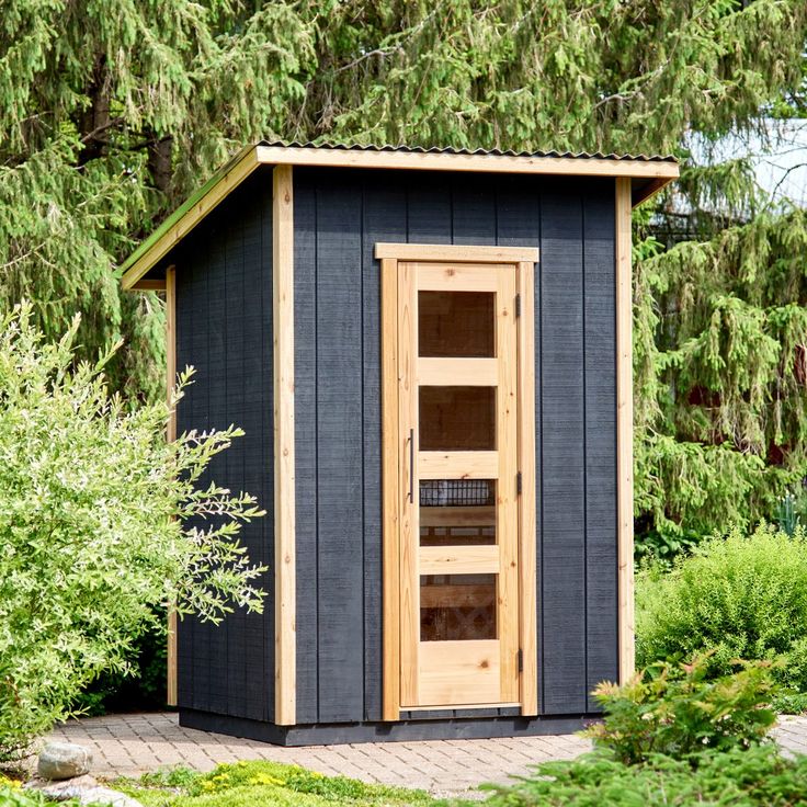 a small wooden outhouse sitting in the middle of a garden with lots of trees