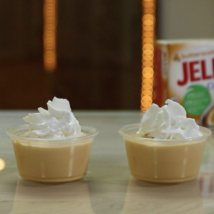 two small cups filled with whipped cream on top of a table next to a can of jello