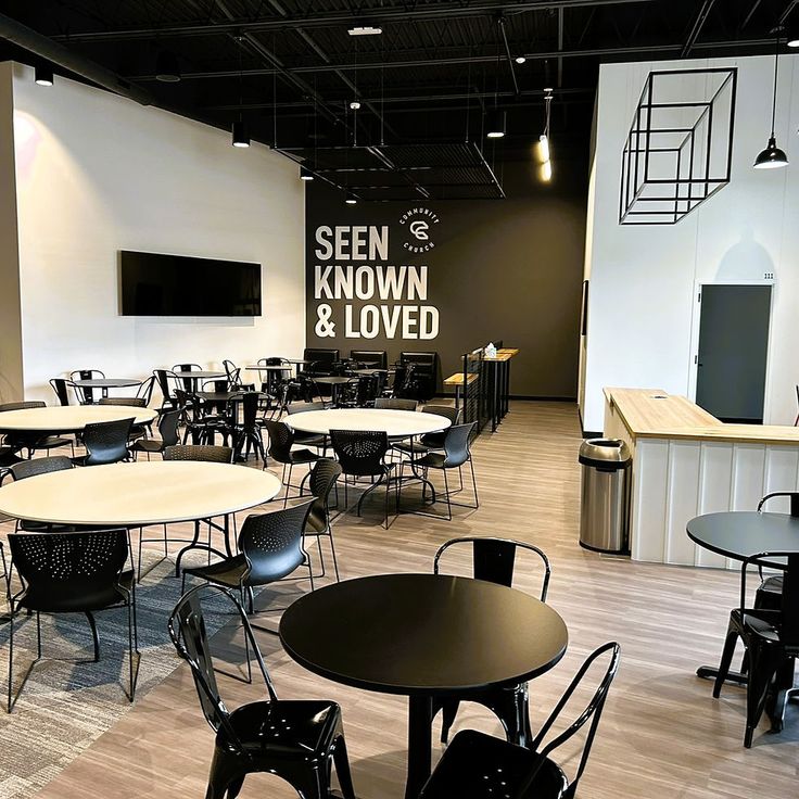 an empty restaurant with tables and chairs in the center, near a wall that says seen known & loved