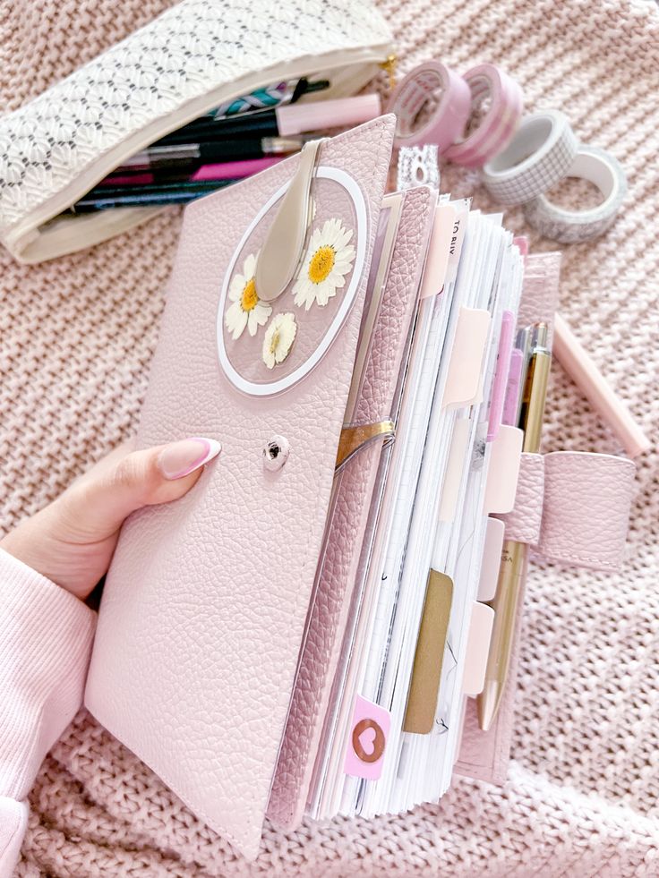 a person holding a pink folder with flowers on it and other items in the background