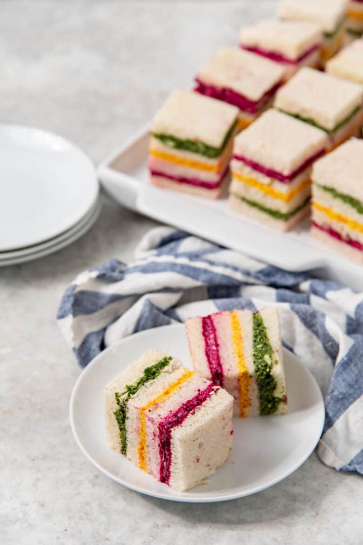 there are many small sandwiches on the plate and one is cut in half to show it's colors