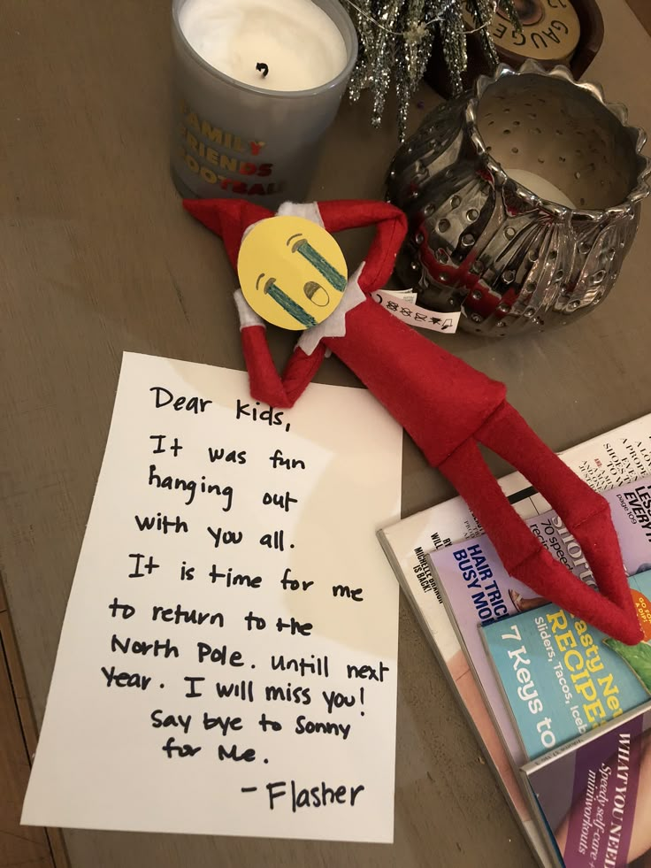 an elf with a note sitting on top of a table next to a candle and some books