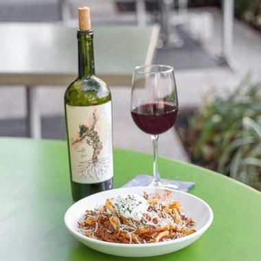 a plate of food and a glass of wine sitting on a table with a bottle of wine in the background