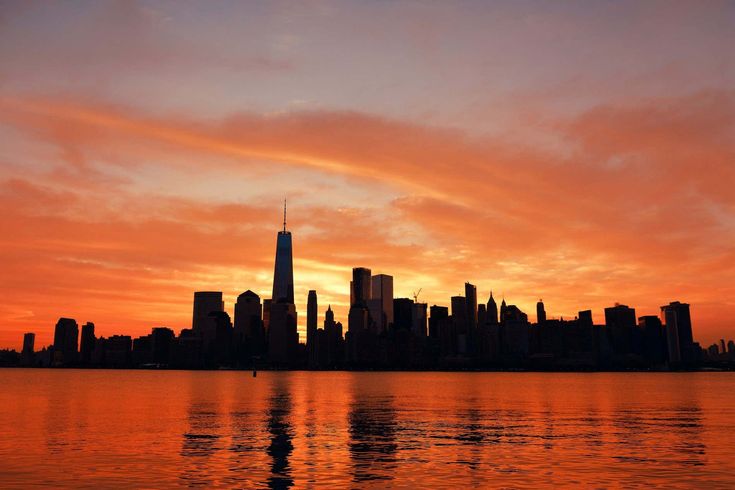 an orange and pink sky is reflected in the water as the sun sets over new york city