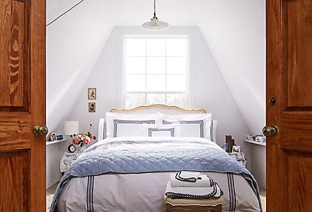 an open door leading to a bed in a room with white walls and wooden floors