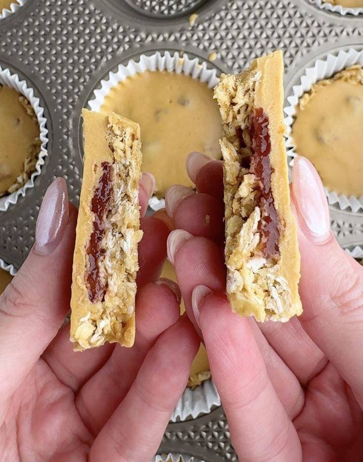 two hands holding food in front of muffin tins filled with peanut butter and jelly