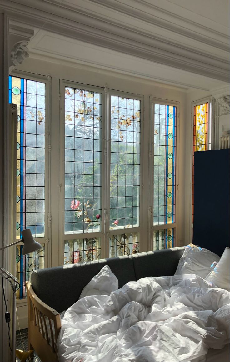 an unmade bed in front of three stained glass windows