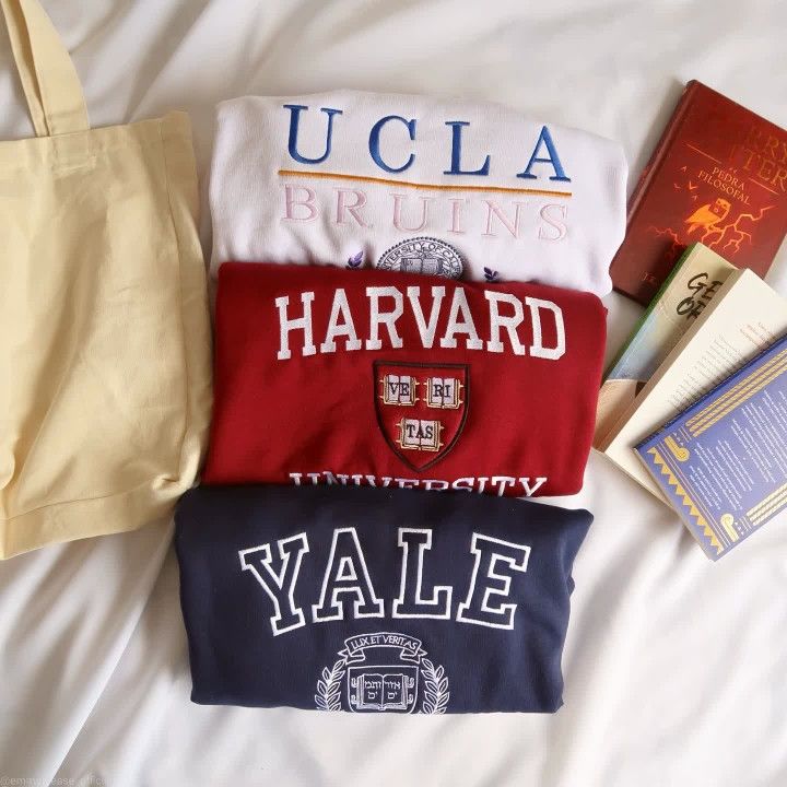 three t - shirts are laid out on a bed with books, and an umbrella