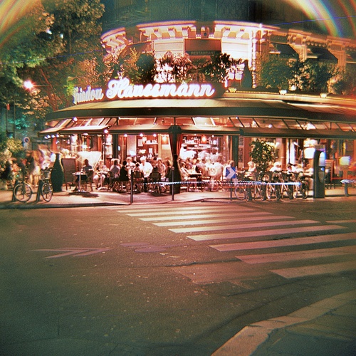 an intersection at night with people walking and riding bikes in front of the storefront