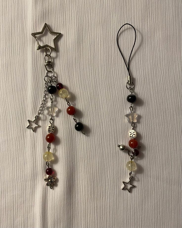 two earrings with beads and charms hanging from them on a white cloth covered tablecloth