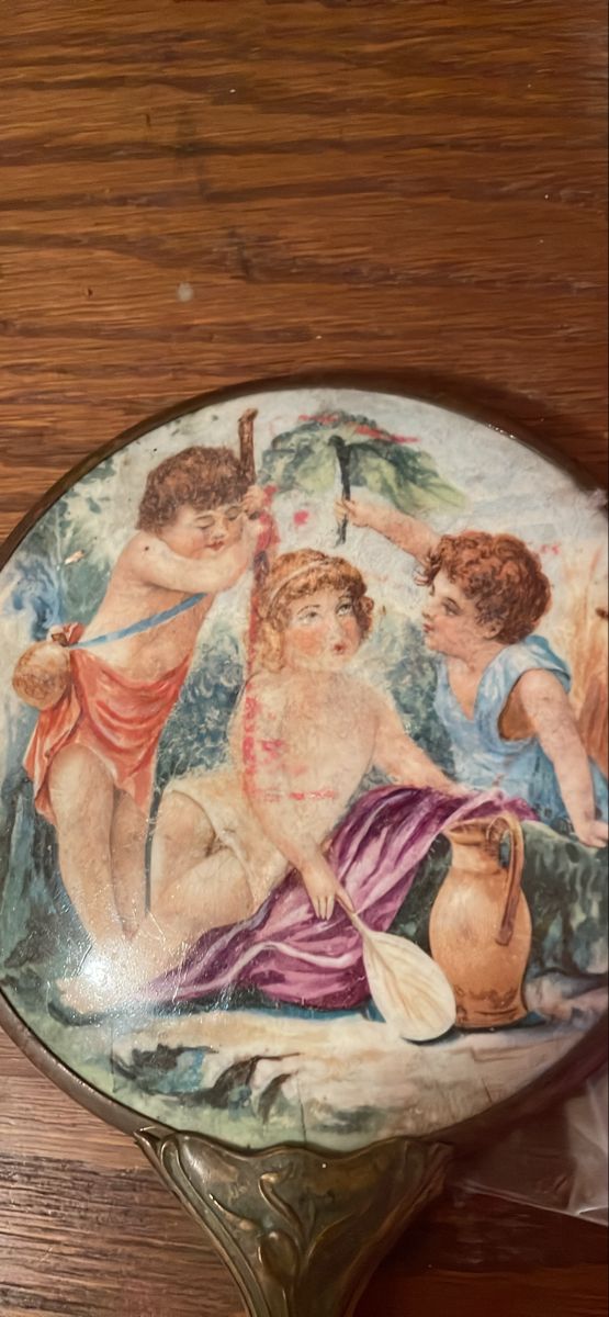 an ornately painted plate on a wooden table with two cherubs and one angel