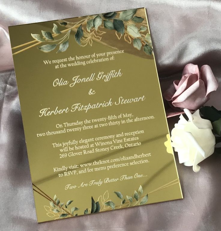 a gold wedding card with flowers on the bed next to it and a pink rose