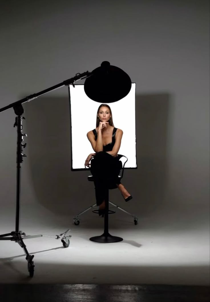 a woman sitting in front of a white screen on top of a chair next to a microphone