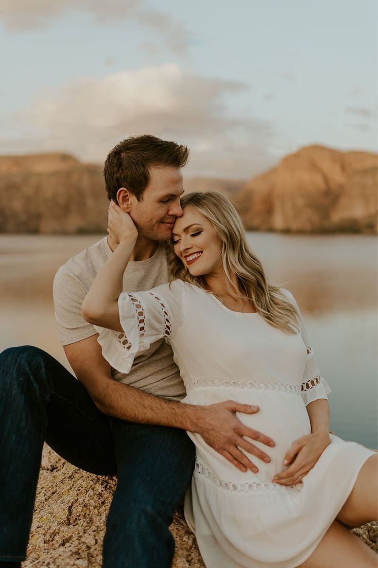 a pregnant couple cuddles on the beach at sunset