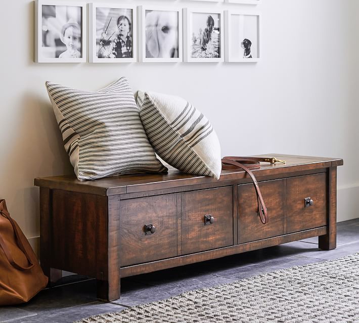 a wooden bench with pillows on it in front of pictures and a handbag sitting next to it