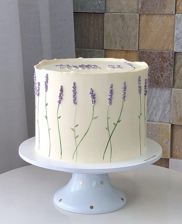 a white cake with lavender flowers on it sitting on a table next to a tile wall