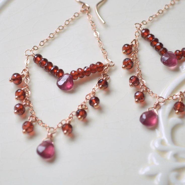 "These dainty garnet chandelier earrings are dripping with sparkly gemstones. In this pair, I have combined red garnets with soft rose gold. The center section is a chevron shape created with small rondelles and rhodolite garnets. More garnets form a fringe at the bottom, which ends in larger, pear-shaped rhodolite garnet. I love the combination of red, raspberry and rose gold, and the repeating triangle shapes give these earrings a modern vibe. This is a great way to wear long earrings without Rhodolite Garnet Jewelry, Jewelry For Teens, Aqua Earrings, Gold Chandelier Earrings, Abalone Earrings, Mermaid Jewelry, Garnet Jewelry, Garnet Earrings, Peridot Gemstone