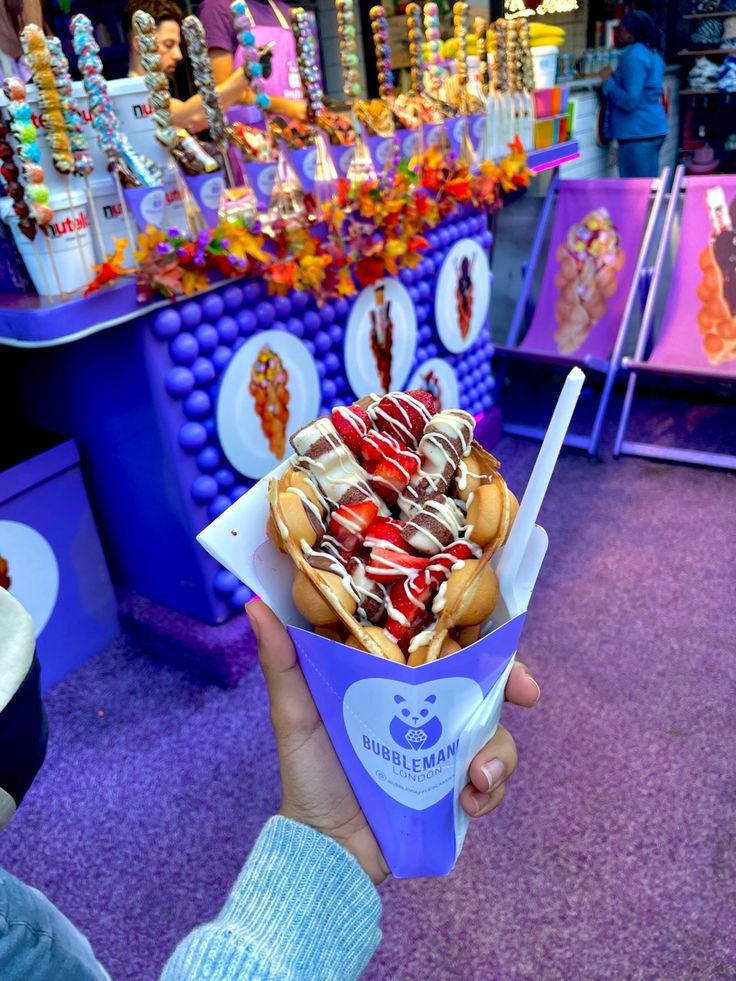 a person holding up a paper cup filled with candy and toppings on top of it