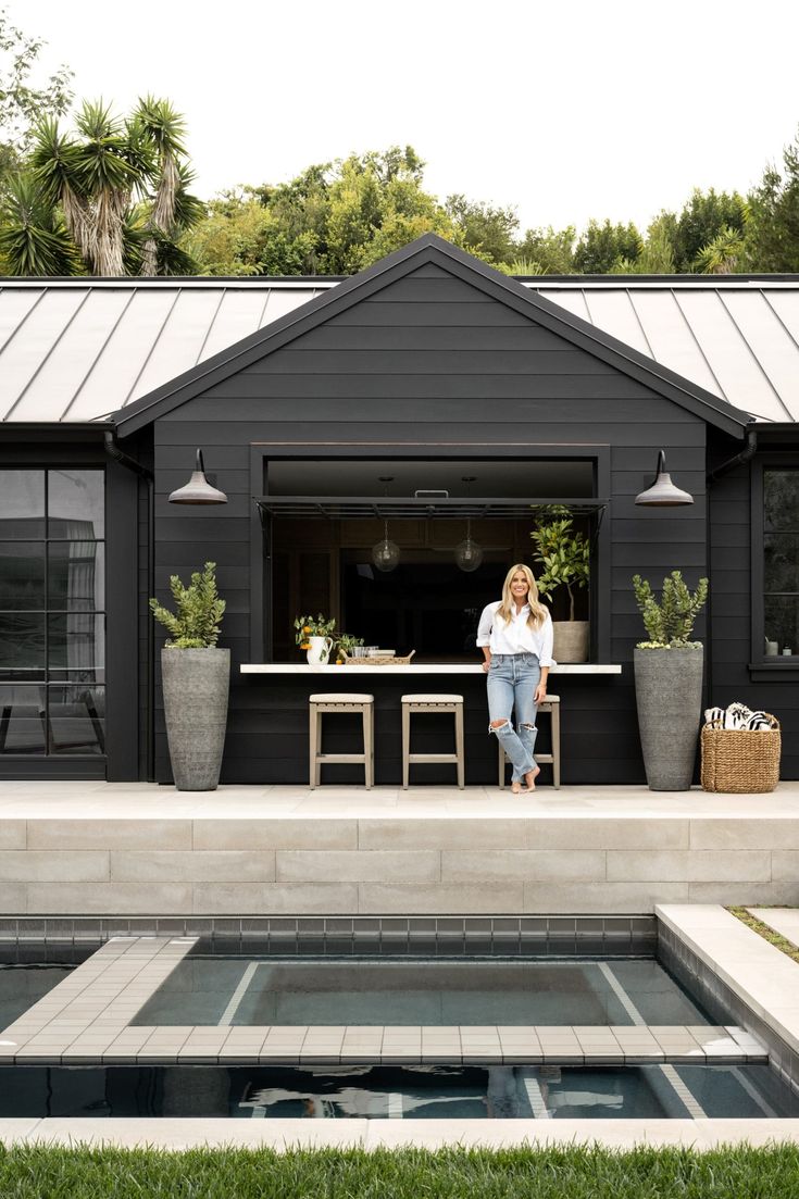 a woman sitting on a bench in front of a house with an outdoor kitchen and dining area