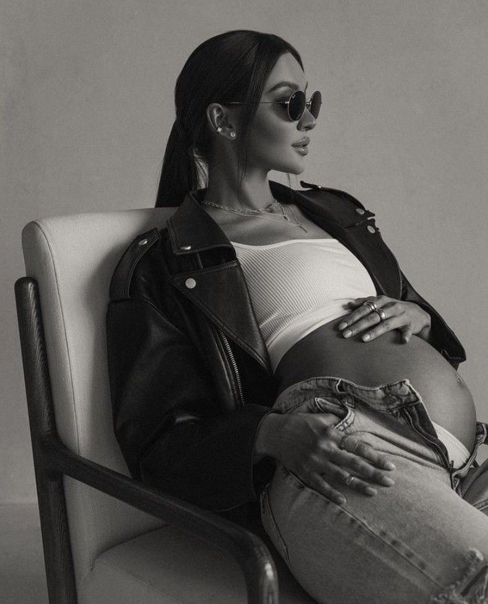 a black and white photo of a pregnant woman sitting in a chair with her hands on her stomach