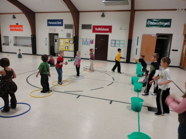 a group of children playing with plastic buckets in a school gym flooring area