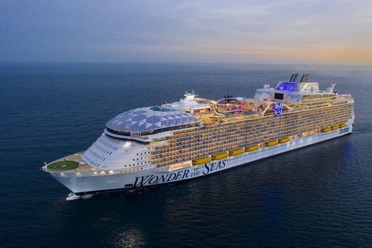 a large cruise ship in the middle of the ocean at sunset with its lights on