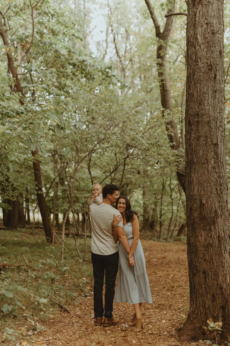 an engaged couple standing next to each other in the woods