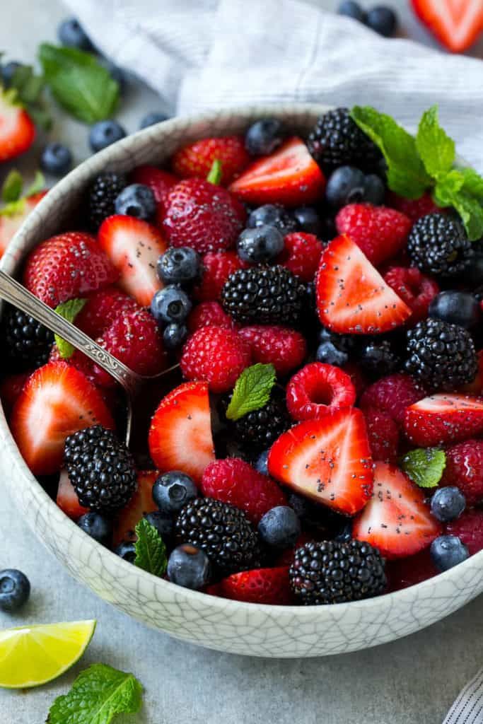 a bowl filled with berries and mint on top of a white cloth next to lemon wedges