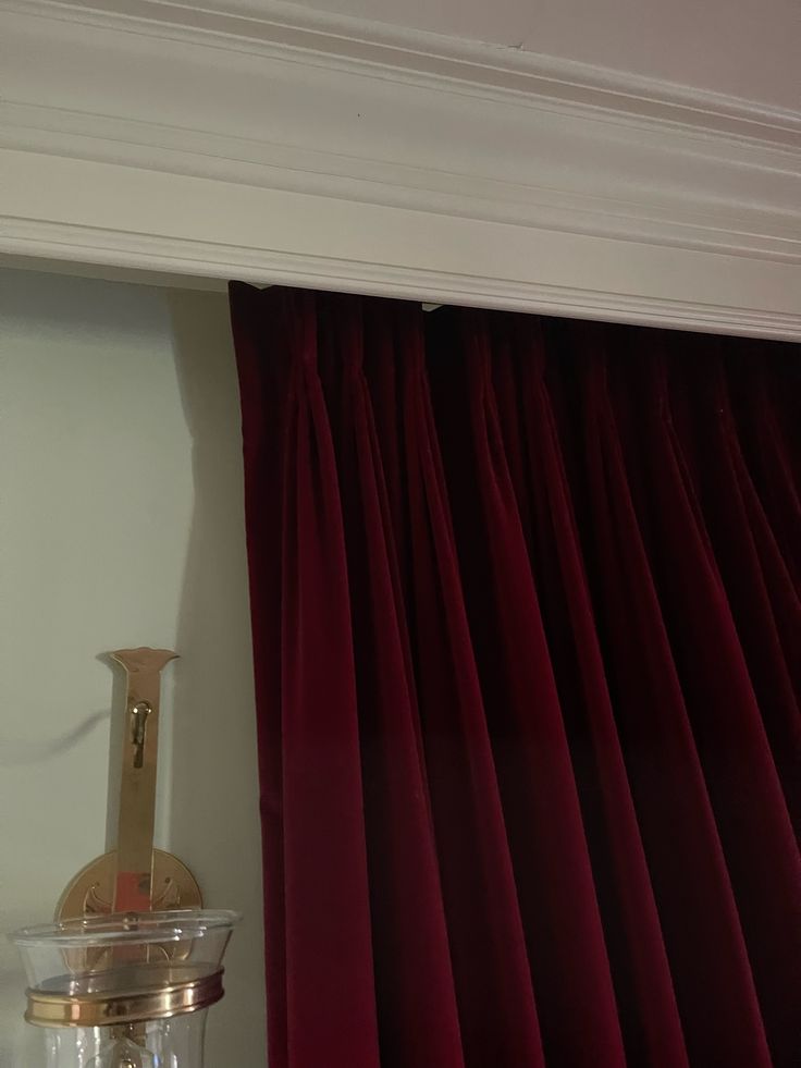 a red curtain hanging from the side of a white wall next to a glass vase