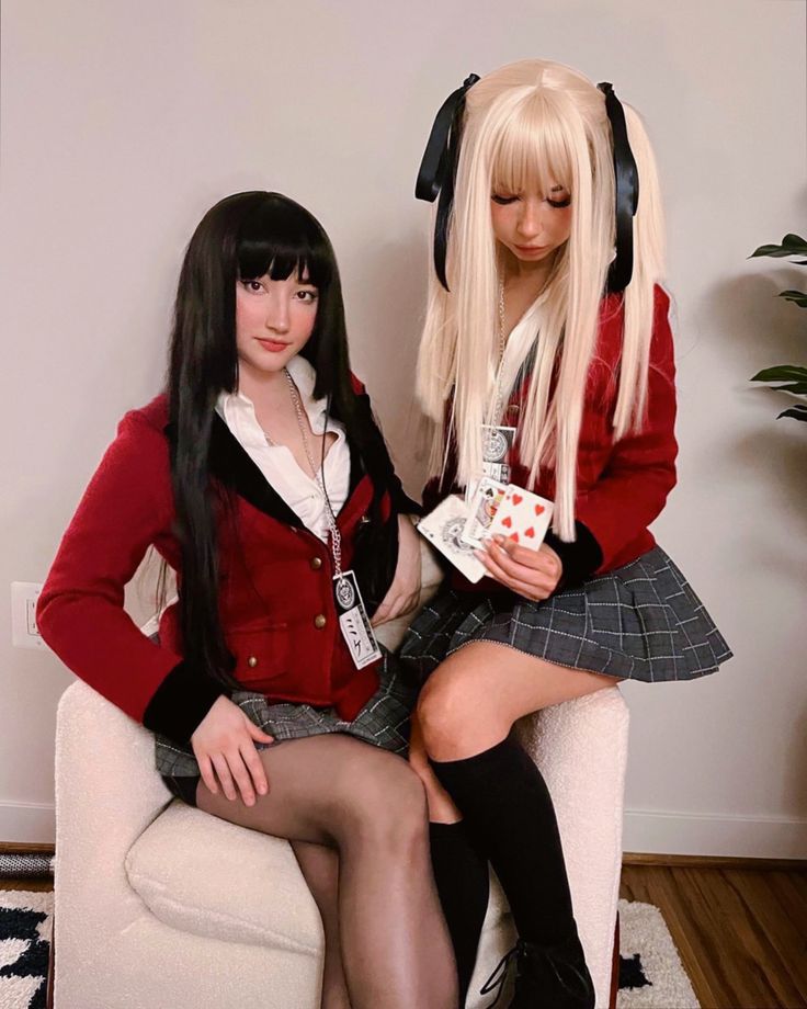 two women sitting on a couch with long black hair and white wigs, one wearing a red sweater