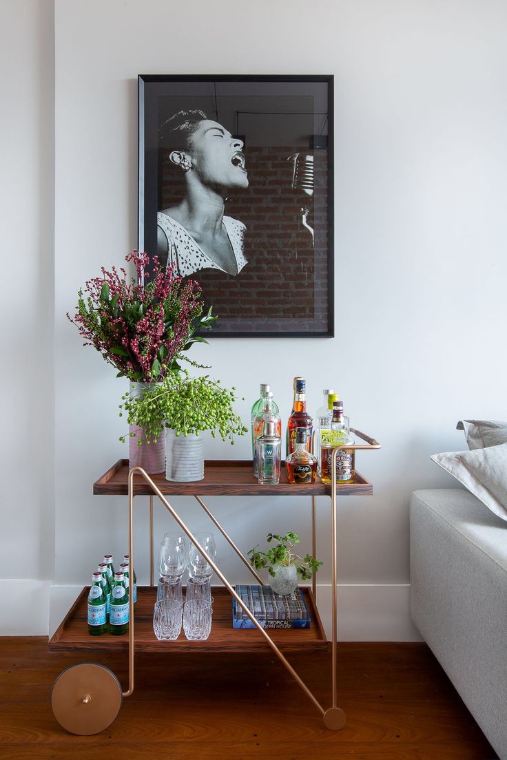 a bar cart with drinks and flowers on it in front of a framed photograph above