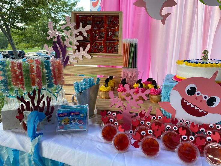 a table topped with cakes and cupcakes covered in frosted icing next to an ocean themed cake