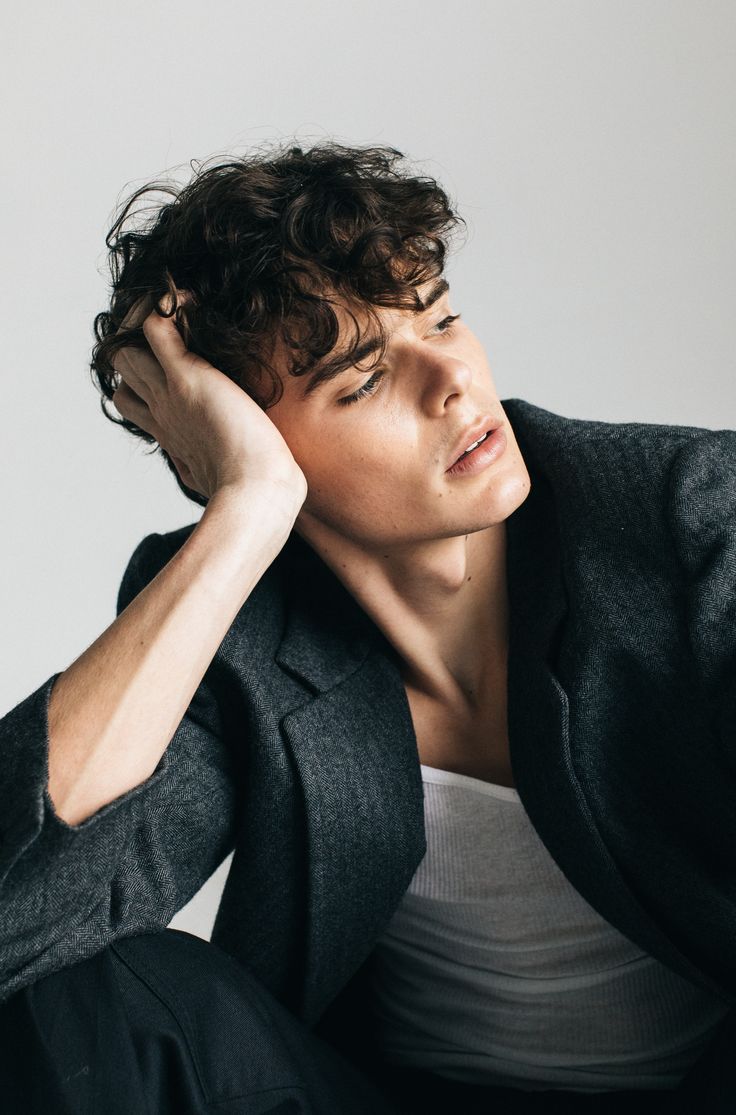 a man with curly hair sitting down and holding his hand to his head while wearing a blazer