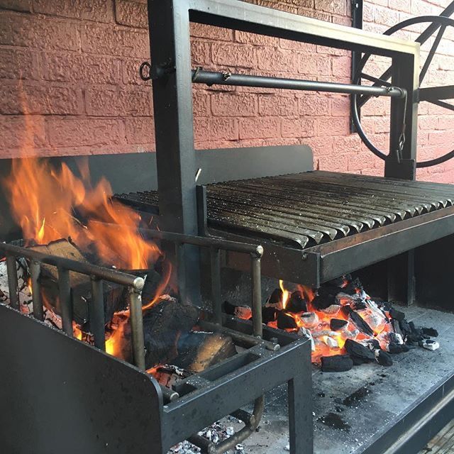 an outdoor grill with fire and flames burning in front of a brick wall behind it