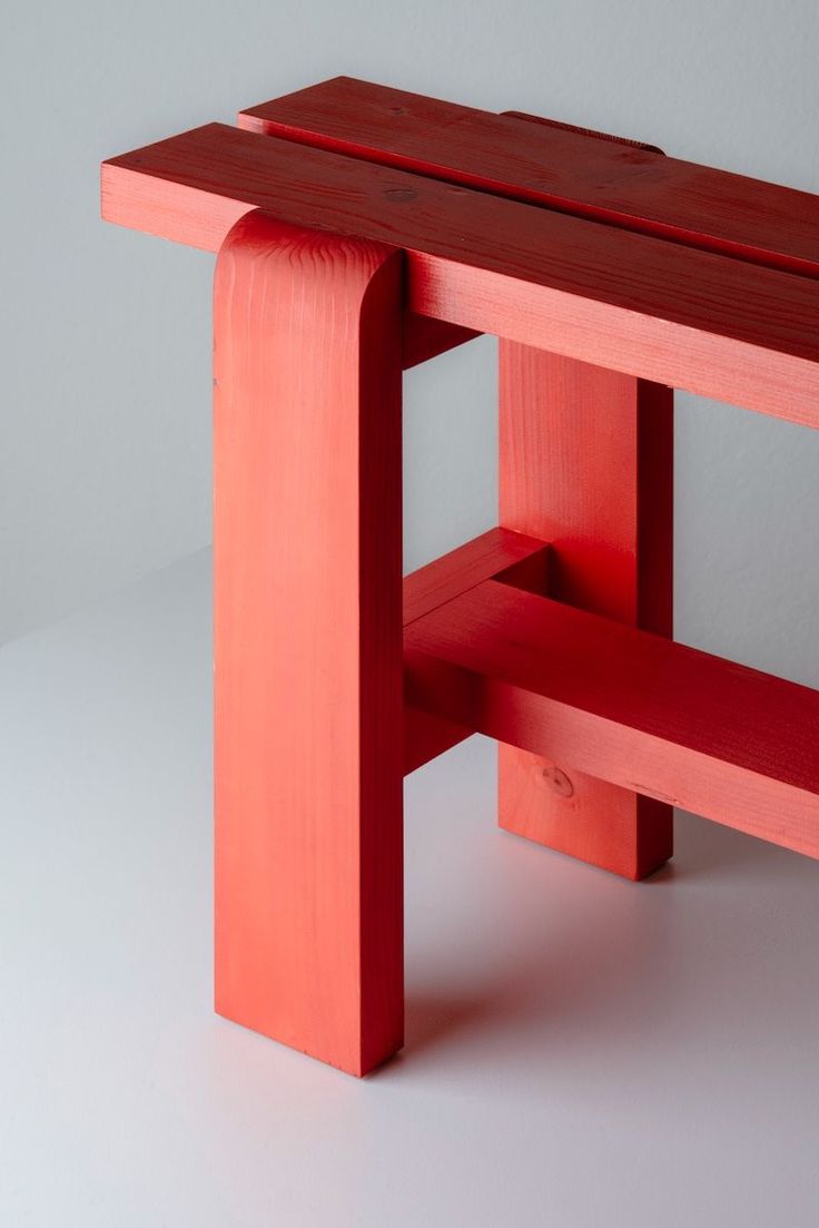 a red wooden bench sitting on top of a white floor next to a gray wall