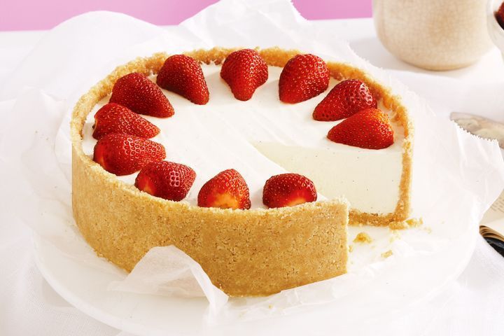 a cheesecake with strawberries on top sits on a plate