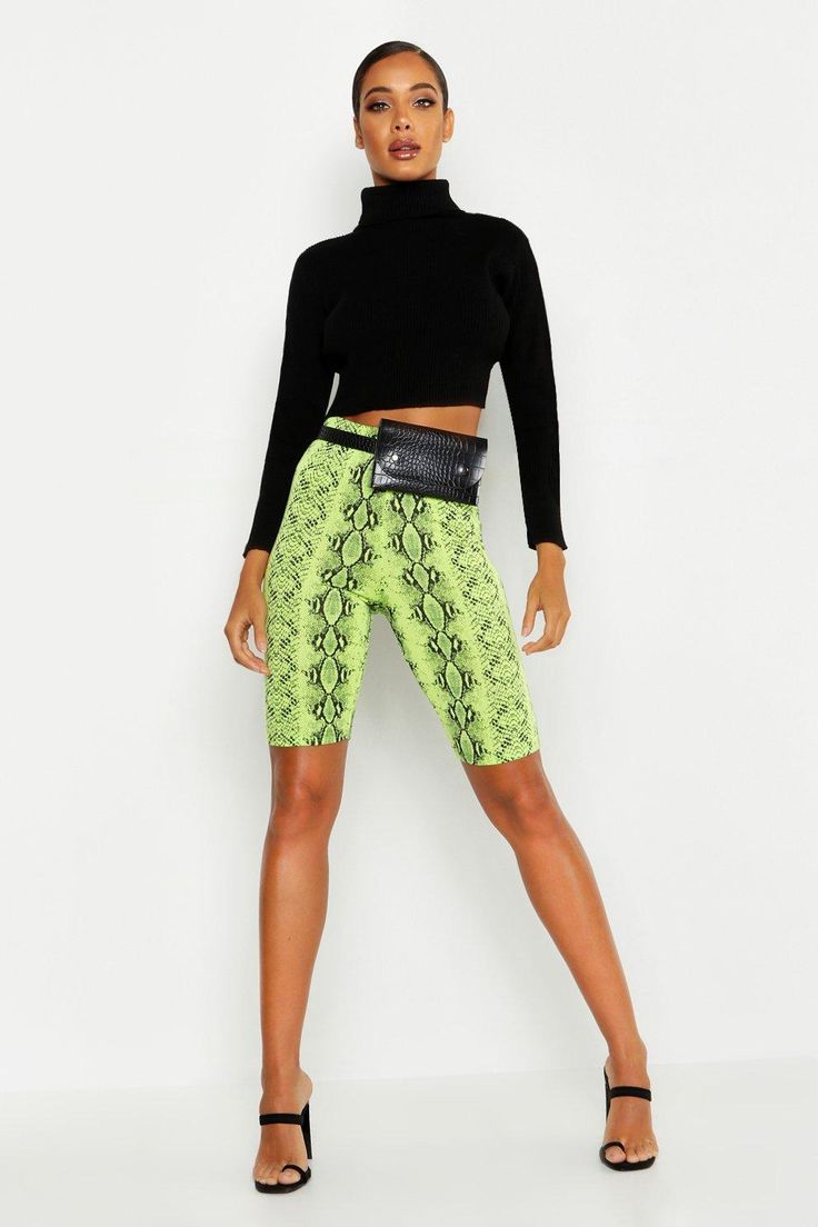 a woman in black top and green snake skin print shorts standing with her hands on her hips