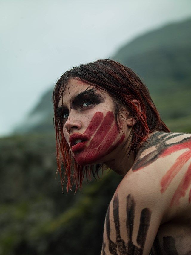 a man with red and black paint on his face is standing in front of mountains