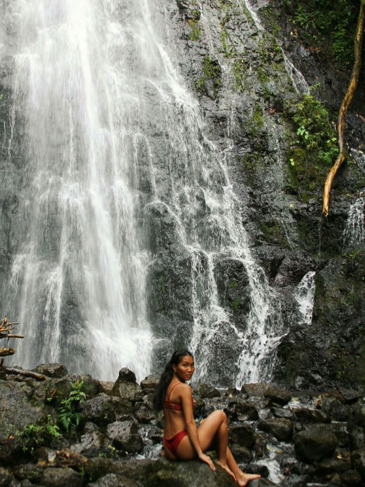 a woman sitting on rocks in front of a waterfall