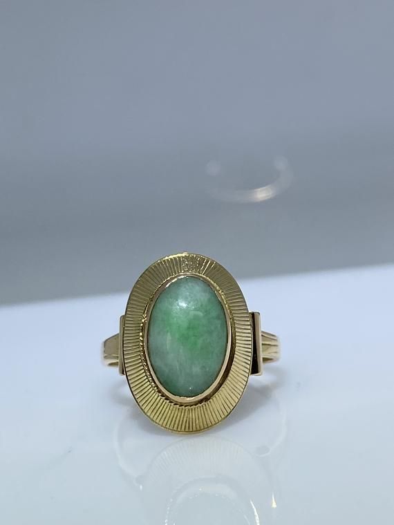 14K yellow gold ring with a natural jade. This vintage piece from the 70’s is delicately made from the top of its scrolled shank to the textured bezel holding the stone in. The oblong oval Jade cabochon is a lovely green hue with white undertones. The basket is nice and opened eliminating any unnecessary weight. It measures 17mm x 12mm across the top and makes for the perfect statement ring. Finger size is 6.5 Feel free to message me if you have any other questions. Oval Jade Rings Hallmarked, Oval Jade Rings In Yellow Gold, Vintage Oval Jade Rings, Vintage Oval Jade Emerald Ring, Vintage Oval Gemstone Signet Ring, Vintage Oval Emerald Ring In 14k Gold, Vintage Jade Rings For Formal Occasions, Vintage 14k Gold Oval Cabochon Emerald Ring, Vintage 14k Gold Emerald Oval Cabochon Ring