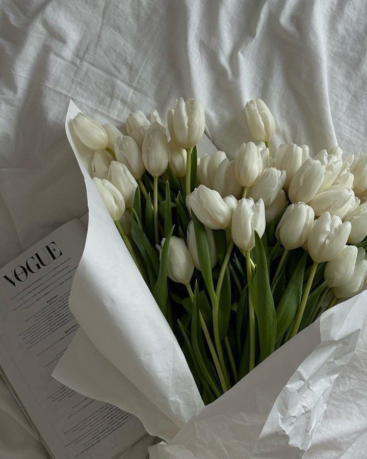 a bouquet of white tulips sitting on top of a bed next to an open book