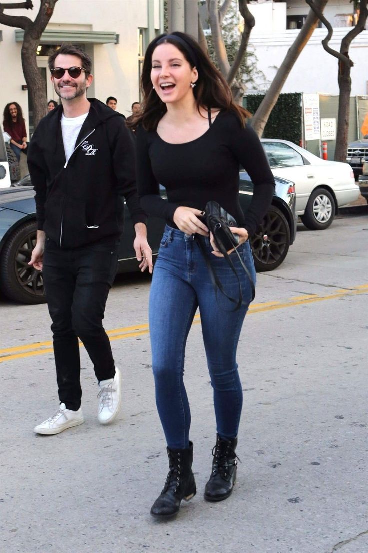 a woman in black shirt and jeans walking down the street with a man behind her