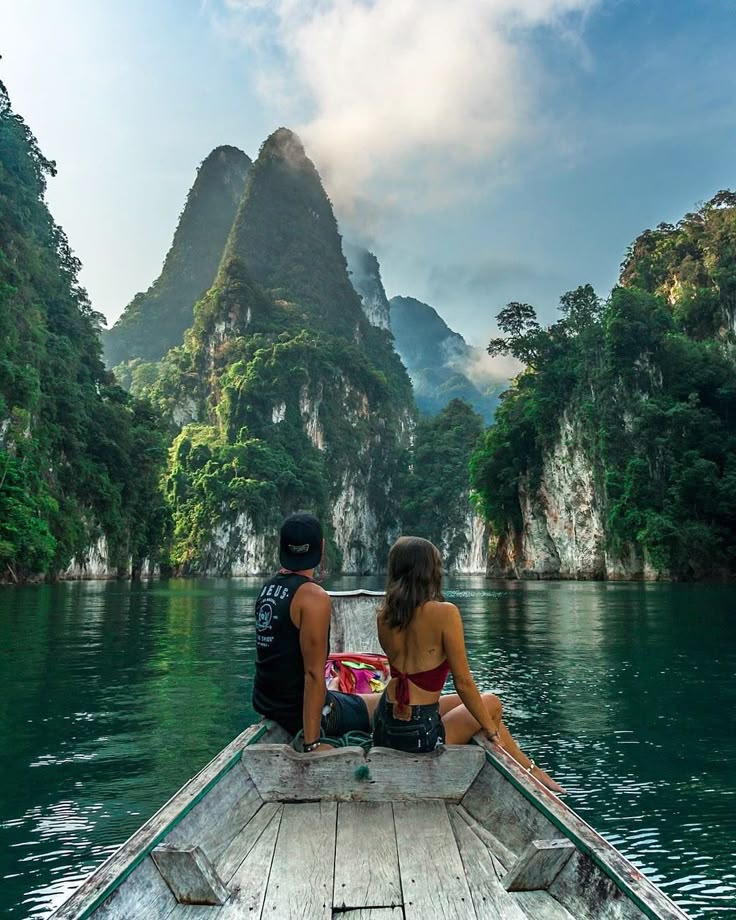 two people are sitting on the back of a boat looking out at mountains and water