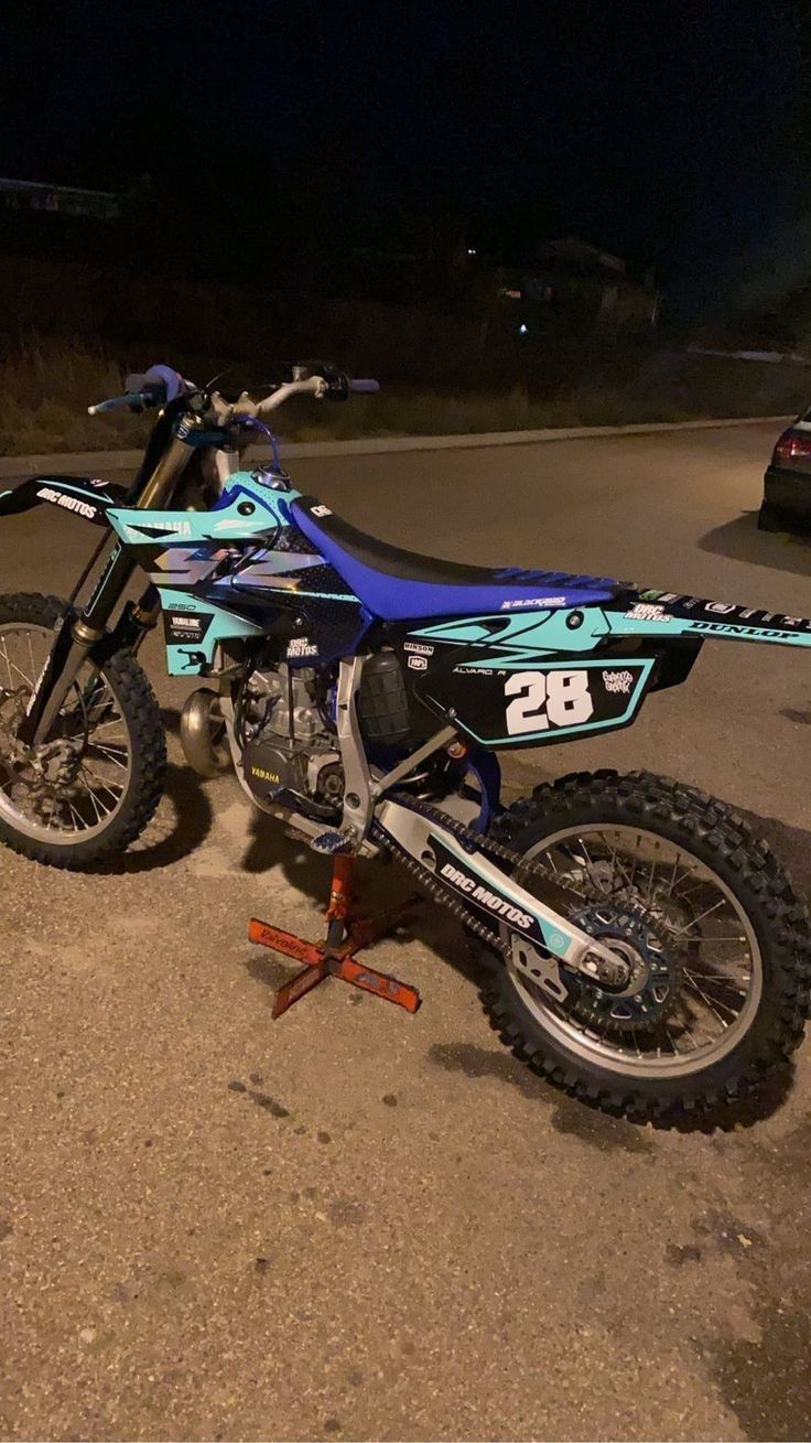 a blue dirt bike parked on the side of a road at night with no one around it