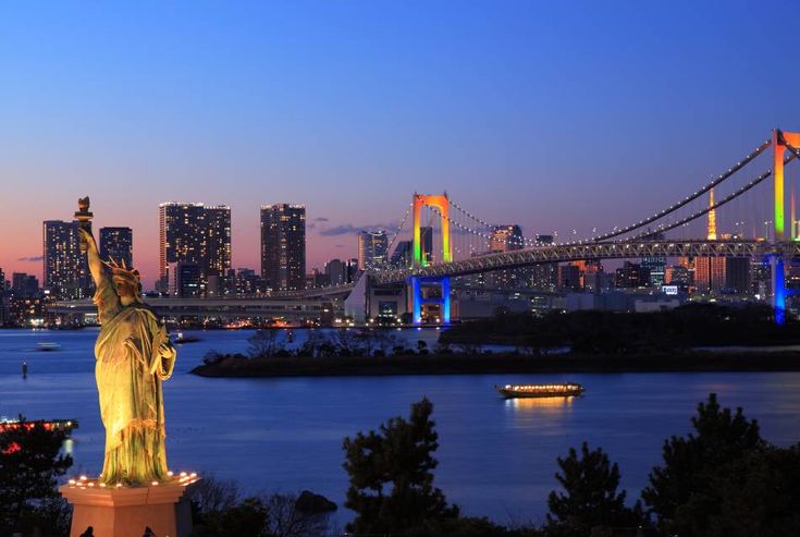 the statue of liberty is lit up at night in front of the bay bridge and city lights