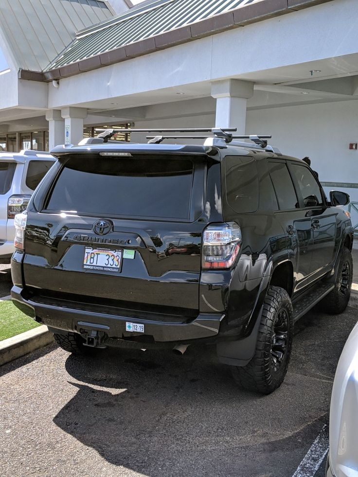 a black toyota suv parked in front of a white building and parking lot with other cars